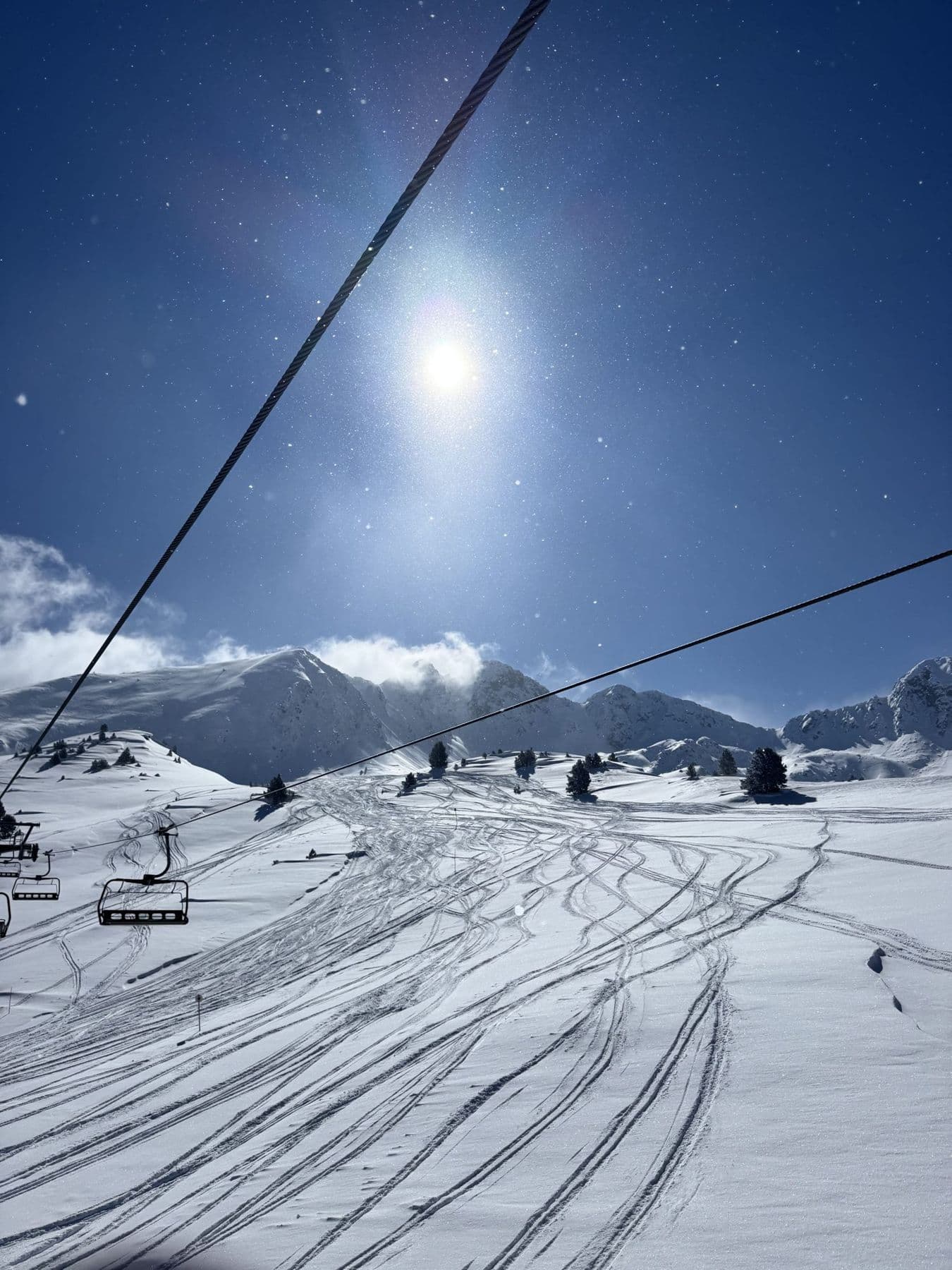 Fresh ski tracks under a bright sun below a chairlift