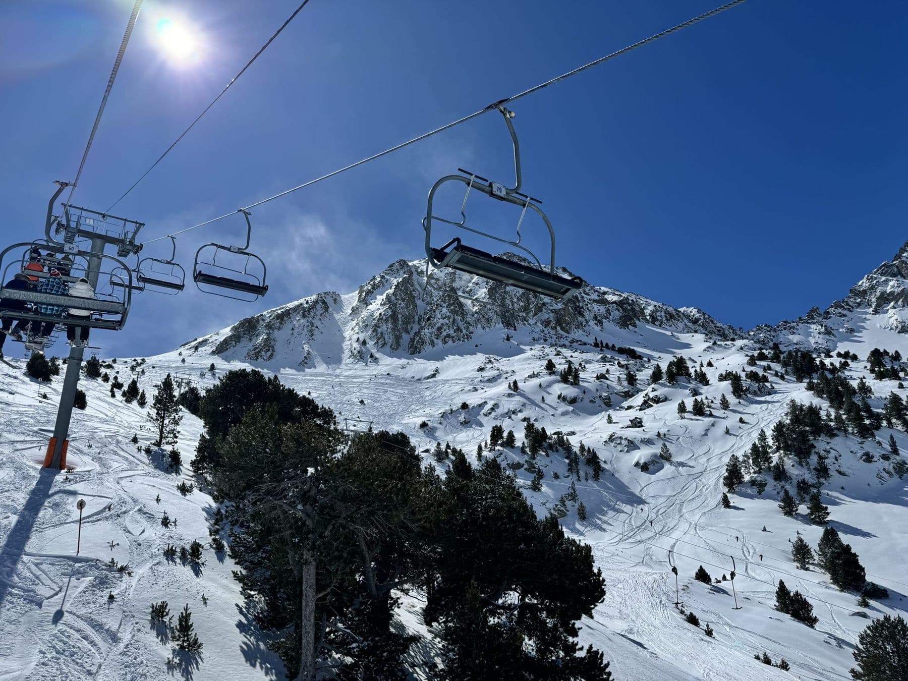 Chairlift over snowy pine slopes and a rocky Pyrenees peak on a bluebird day