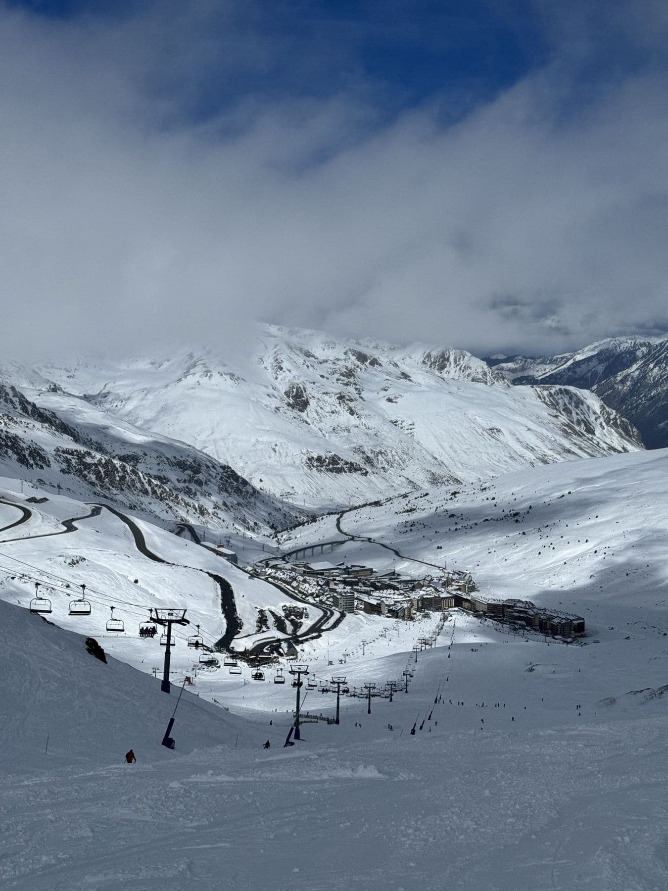 A snowy Pyrenees valley with lifts and a village below the clouds